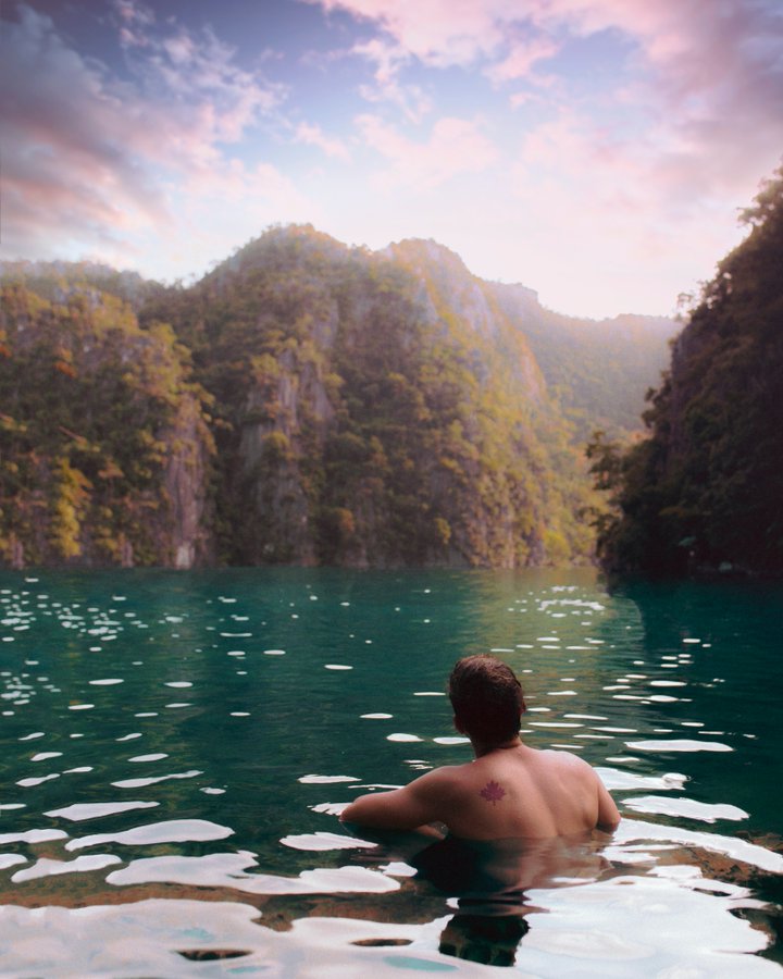 photo tropical location a man half submerged in water looks out away from the camera to a blue lagoon and green mountains